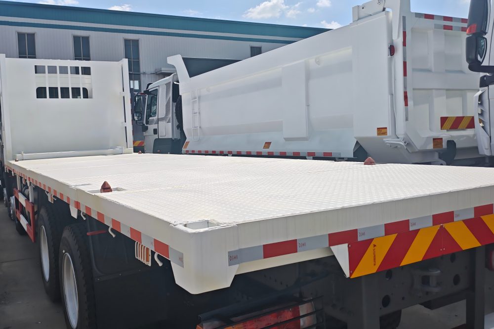 HOWO 8x4 Flatbed Truck carrying heavy construction machinery and industrial equipment on a reinforced steel cargo platform
